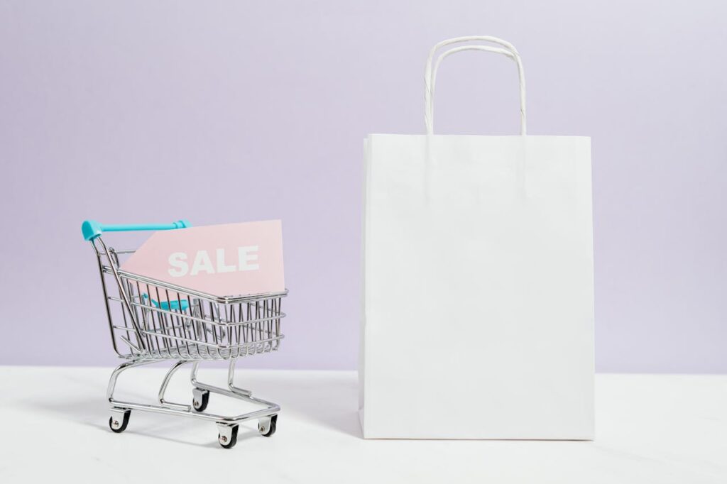 A miniature shopping cart with a sale sign beside a paper bag, perfect for online shopping themes.